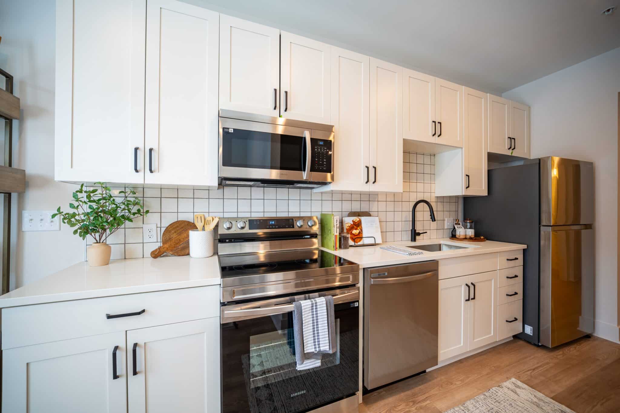 Modern kitchen with white cabinets, stainless steel appliances, a black refrigerator, and a countertop with various kitchen items and a small potted plant.