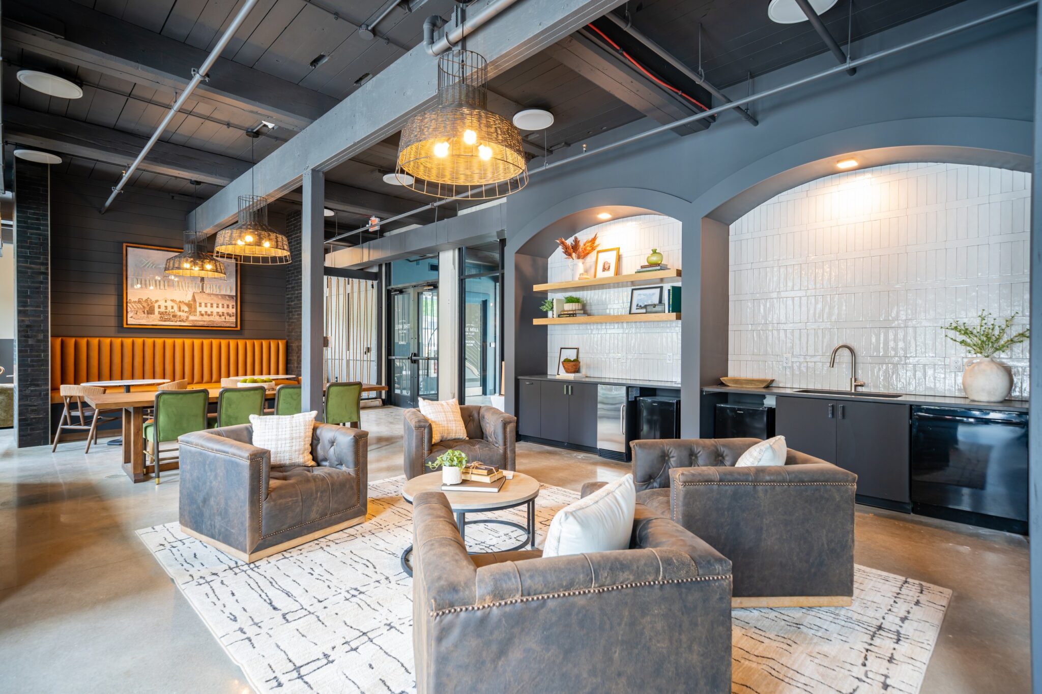 Modern lounge area with leather armchairs, a rug, and a dining table in an open space featuring a kitchenette and industrial-style lighting.