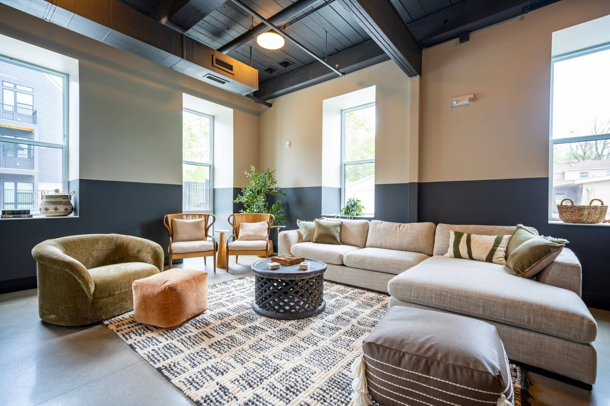 A modern living room with a large sectional sofa, armchairs, a round coffee table, an area rug, and large windows letting in natural light.