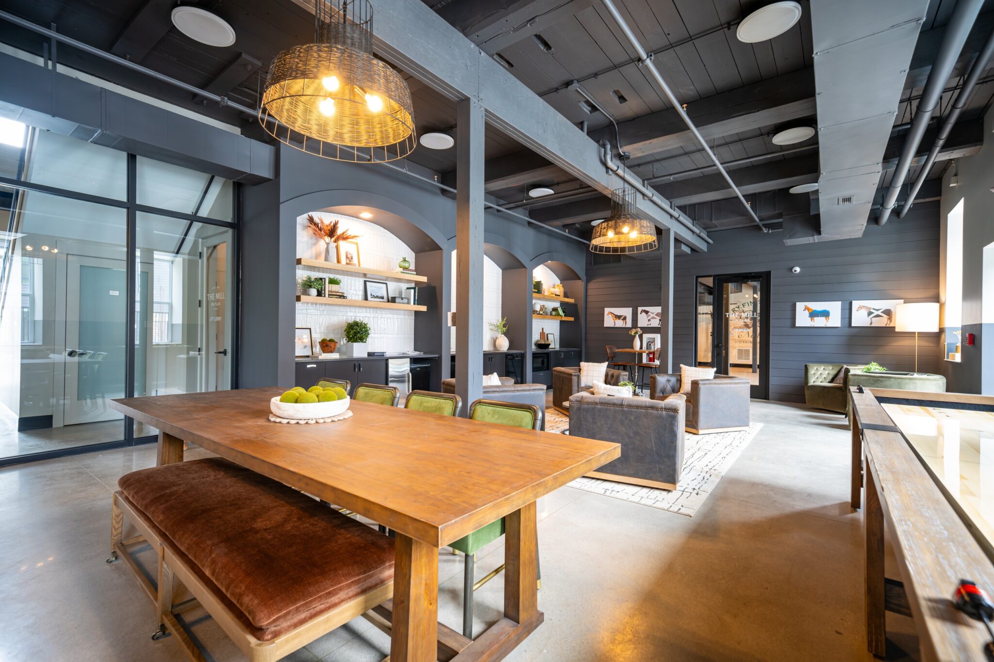 Modern open-concept lounge with wooden dining table, green chairs, cozy seating area, exposed beams, and industrial lighting fixtures.