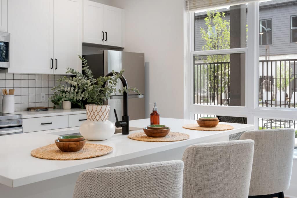 Modern kitchen with white cabinets, stainless steel appliances, and a large island set for three—bringing a touch of mill on flax charm alongside a window that fills the space with natural light.