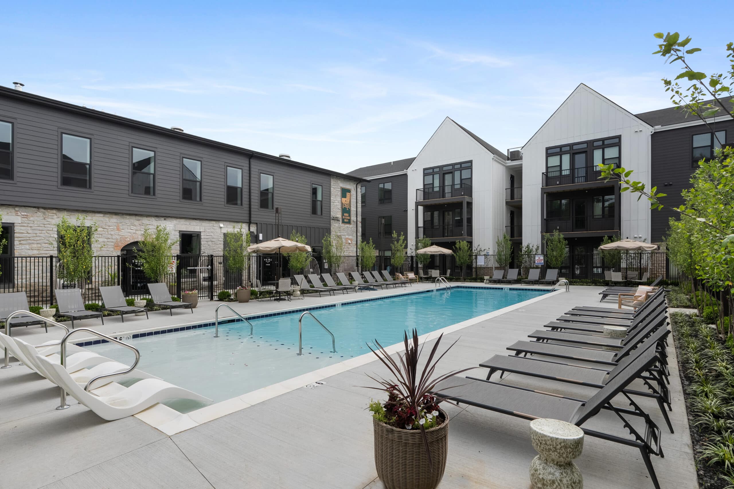 Modern apartment complex at Mill on Flax with an outdoor swimming pool, lounge chairs, umbrellas, and landscaped surroundings on a clear day.