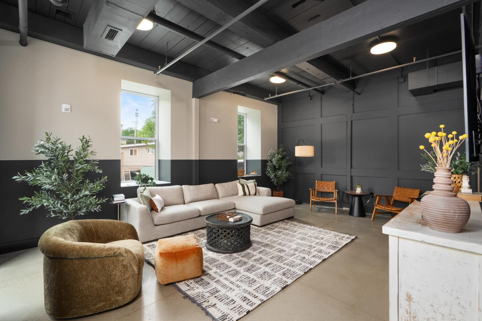 Modern living room with a gray sectional sofa, olive green chair, patterned rug, and dark accent wall, featuring large windows and minimalist decor inspired by the refined textures of a mill on flax.