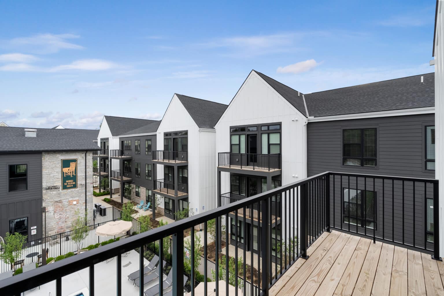 Experience urban convenience at The Mill on Flax from your balcony, overlooking a modern apartment complex with black railings, white and gray exteriors, and landscaped common areas under a blue sky.
