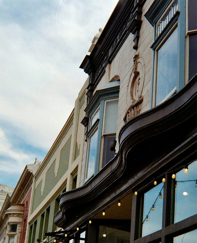 A close-up view of a historic building facade with ornate architectural details, large windows, and string lights highlights the charm and amenities offered, all set under a partly cloudy sky.