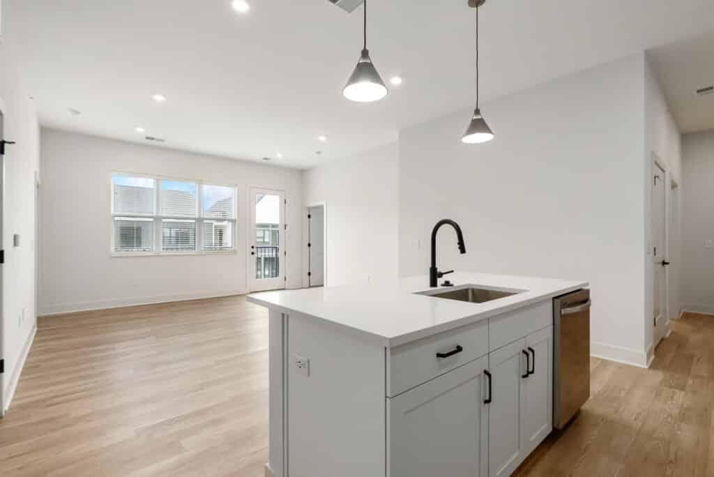 Modern, unfurnished two bedroom apartment featuring an open-plan kitchen and living area with light wood floors, white walls, and large windows providing natural light.