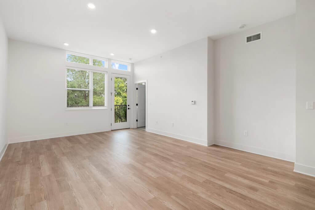 Unfurnished one bedroom apartment featuring light wood flooring, white walls, a large window, glass door to a balcony, and recessed ceiling lights.