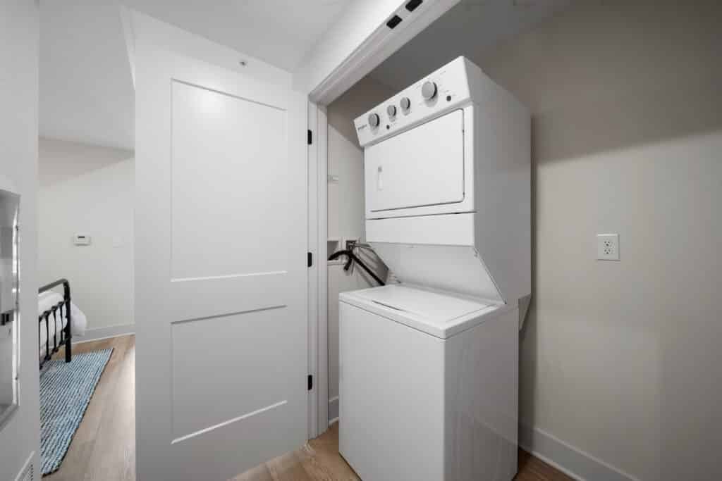 A white stacked washer and dryer unit is installed in a laundry closet with a partially open white door, perfectly suited for a modern studio apartment.